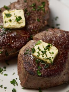 Two sous vide filet mignon steaks on a white plate topped with butter.