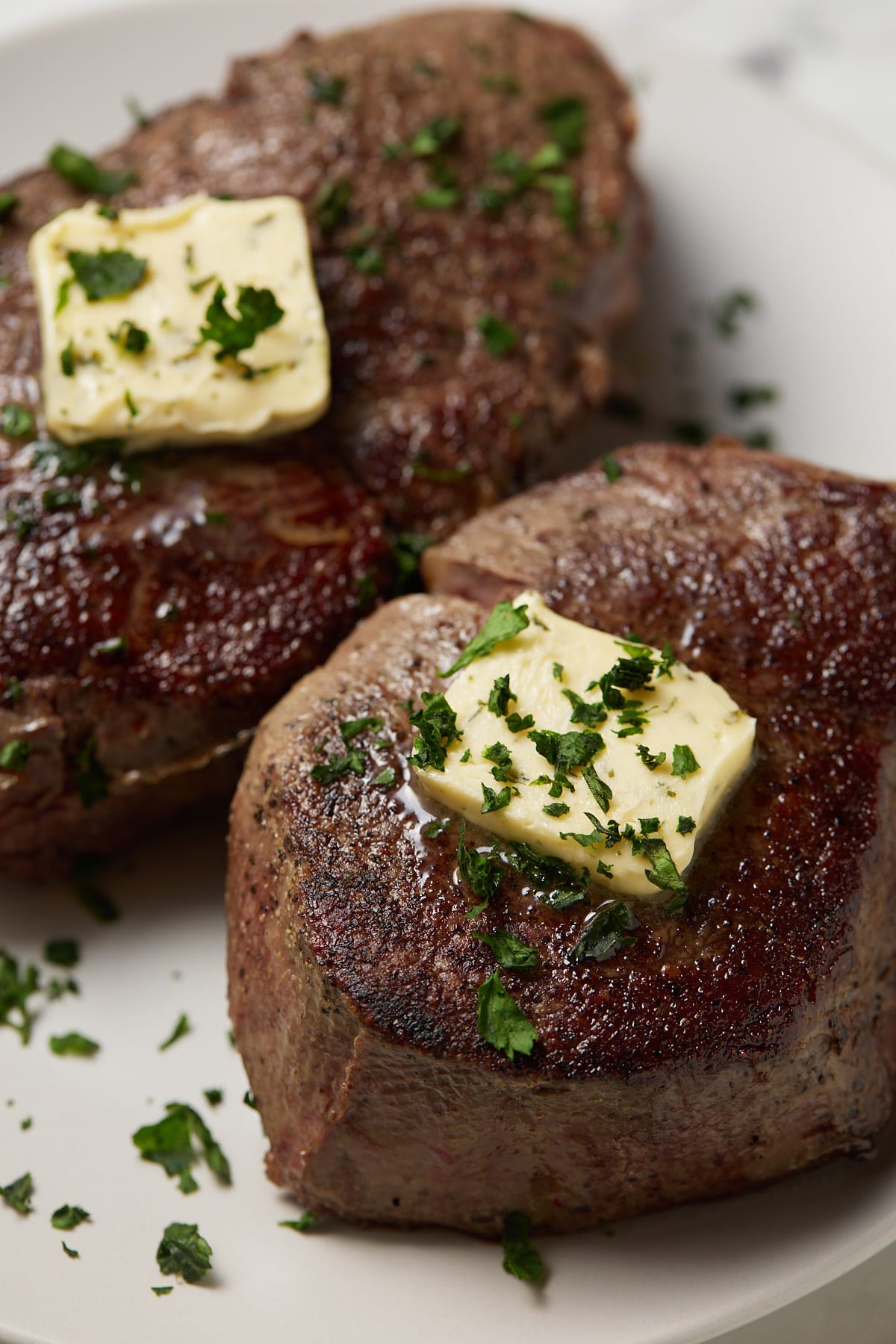 Two sous vide filet mignon steaks on a white plate topped with butter.