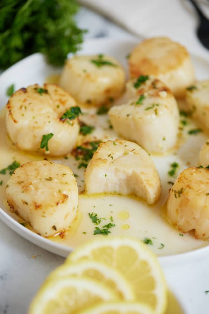 Air fryer scallops on a serving plate with a bite taken out of one.