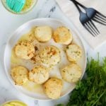 Nine cooked scallops on a white plate.