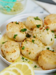 Cook scallops on a white plate next to slices of lemon.