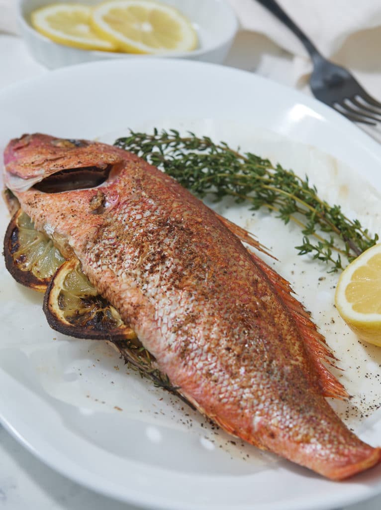 Whole fish served on a plate with thyme and fresh lemons.