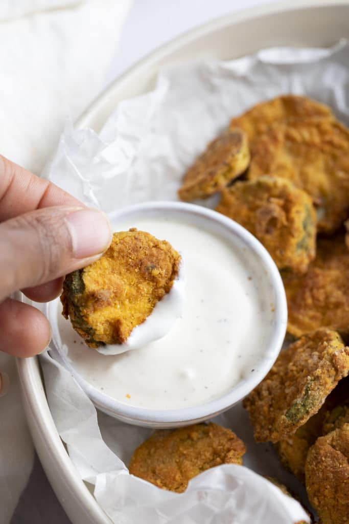 A fried pickle being dipped in a creamy dip.