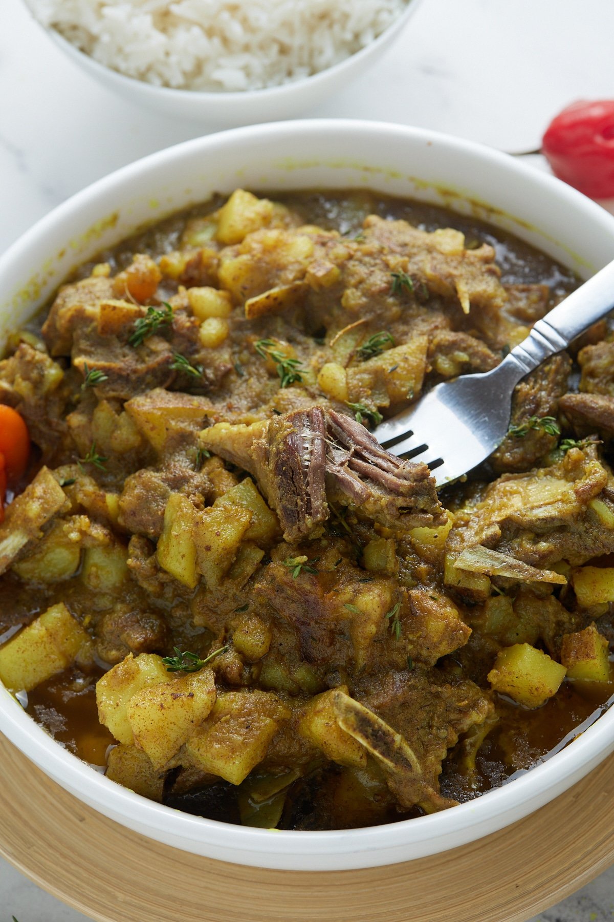 curry goat with fork in white bowl