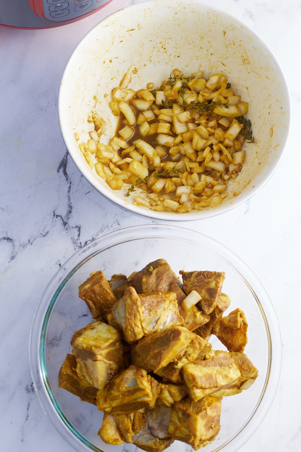 2 white bowls, 1 with onions and seasonings and the other with goat with seasonings