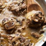 A wooden spoon lifting up one of the salisbury steaks.