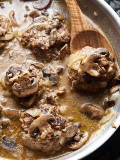 A wooden spoon lifting up one of the salisbury steaks.