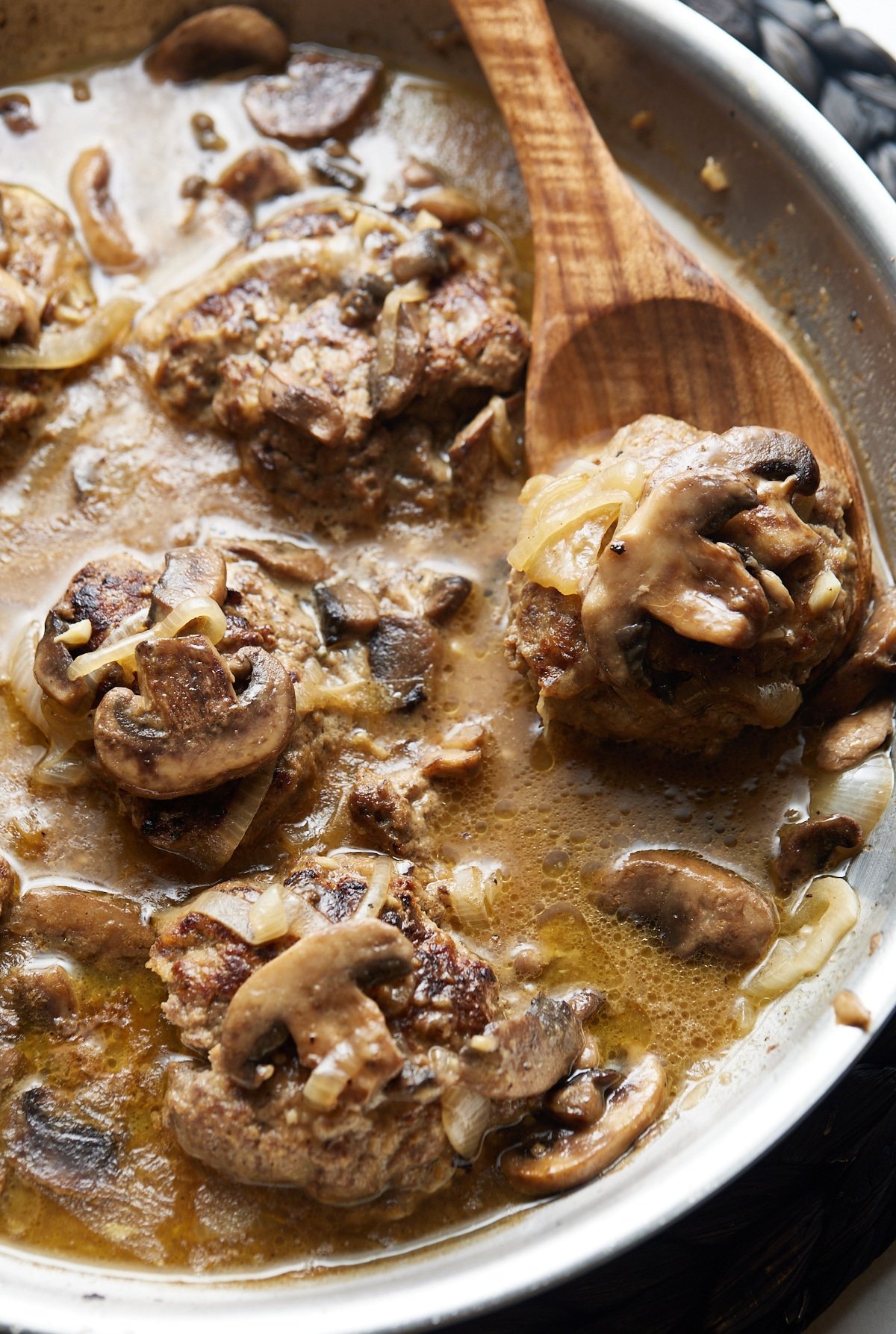 A wooden spoon lifting up one of the salisbury steaks.