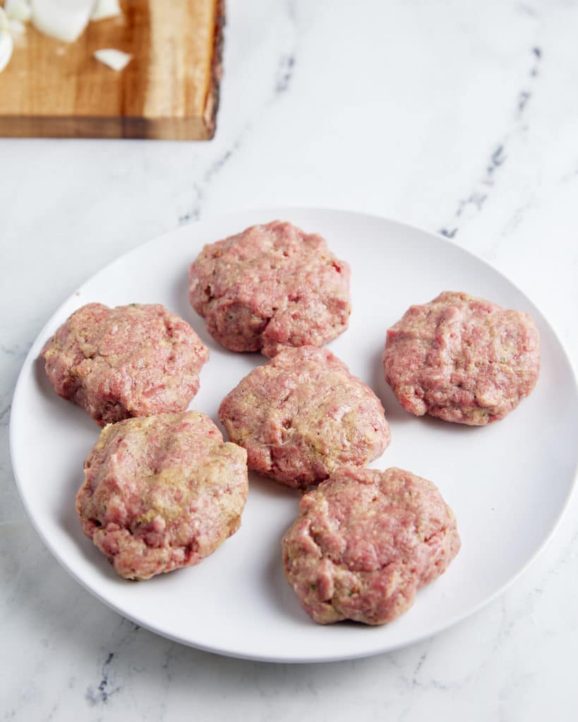 Six beef patties on a white plate.