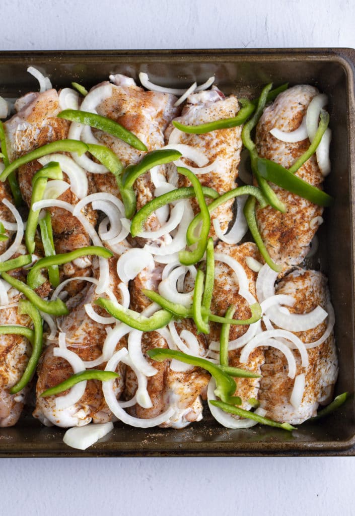 Sliced onions and peppers on the turkey wings in the roasting tin.