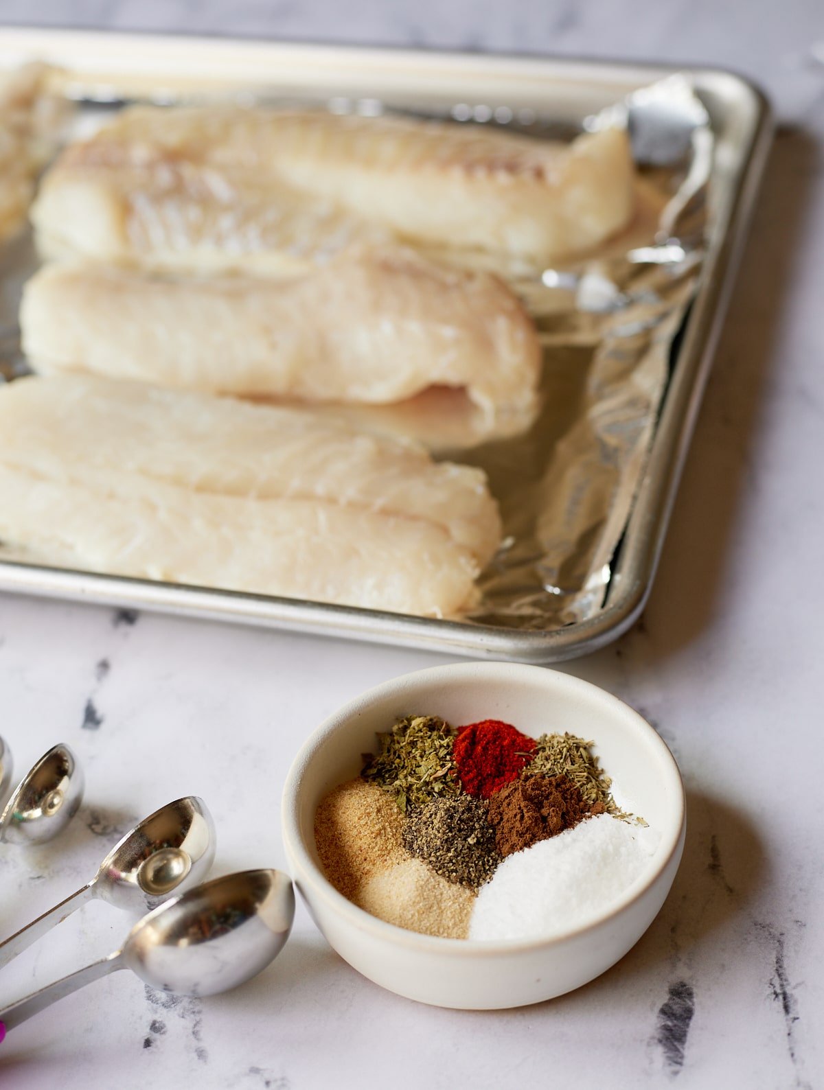 Herbs and spices in a bowl next to fish fillets.