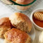 Three honey whole wheat dinner rolls on a white plate.