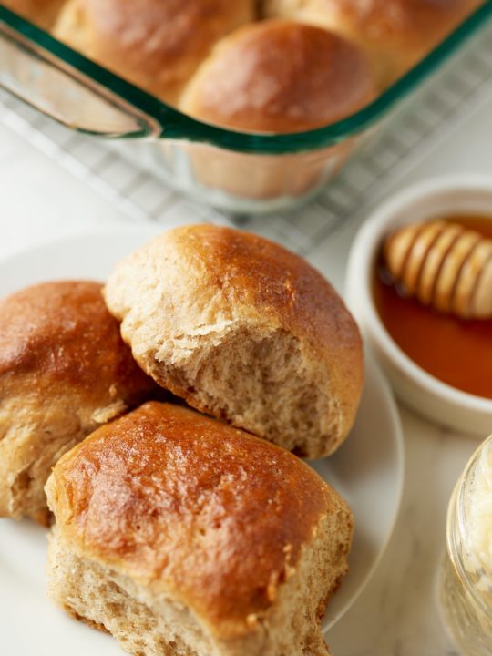 Three honey whole wheat dinner rolls on a white plate.