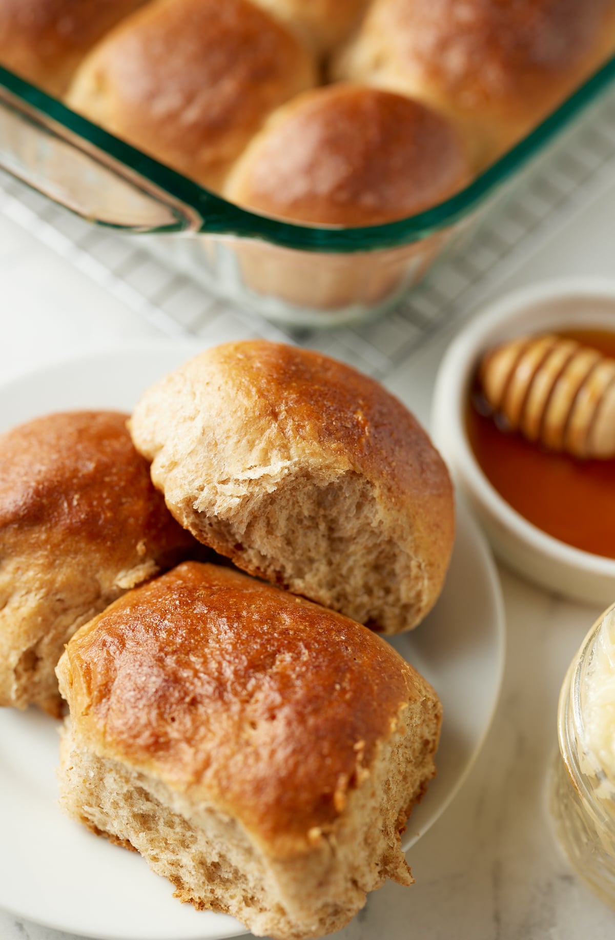 Three honey whole wheat dinner rolls on a white plate.