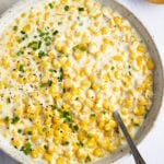 A spoon in a skillet of creamed corn.