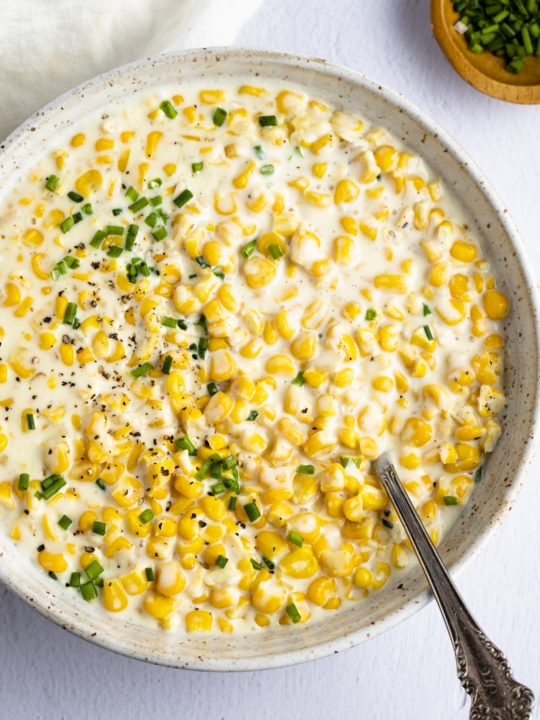 A spoon in a skillet of creamed corn.