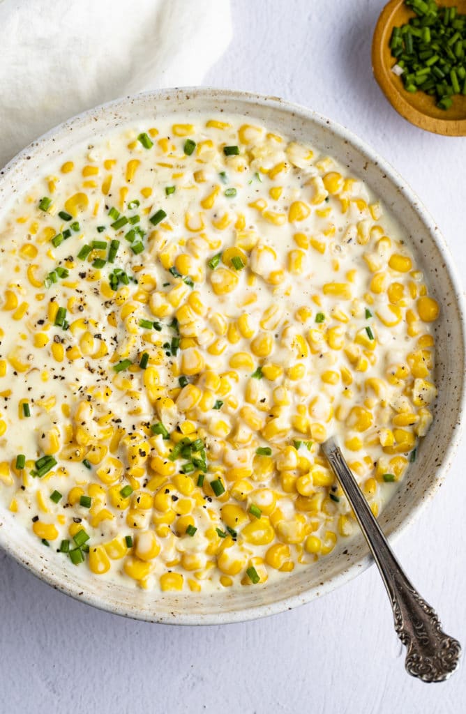 A spoon in a skillet of creamed corn.