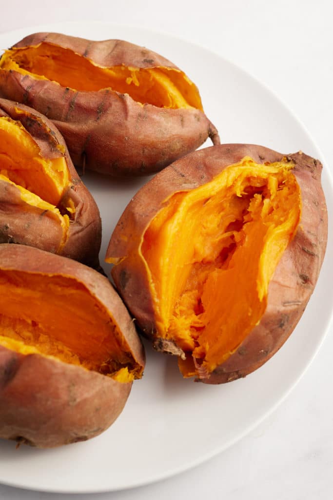 Four sweet potatoes on a white plate cut in half.