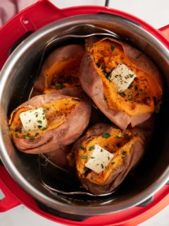 Cooked sweet potatoes in an Instant Pot, split open and topped with butter and fresh herbs.