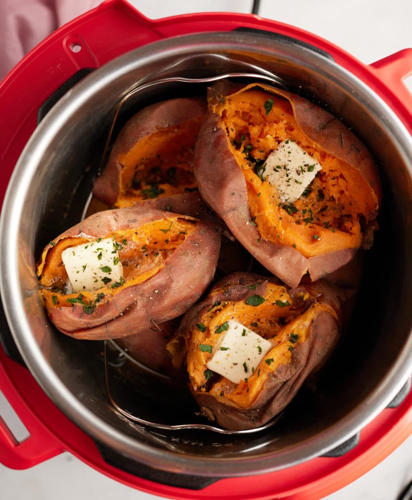Cooked sweet potatoes in an Instant Pot, split open and topped with butter and fresh herbs.