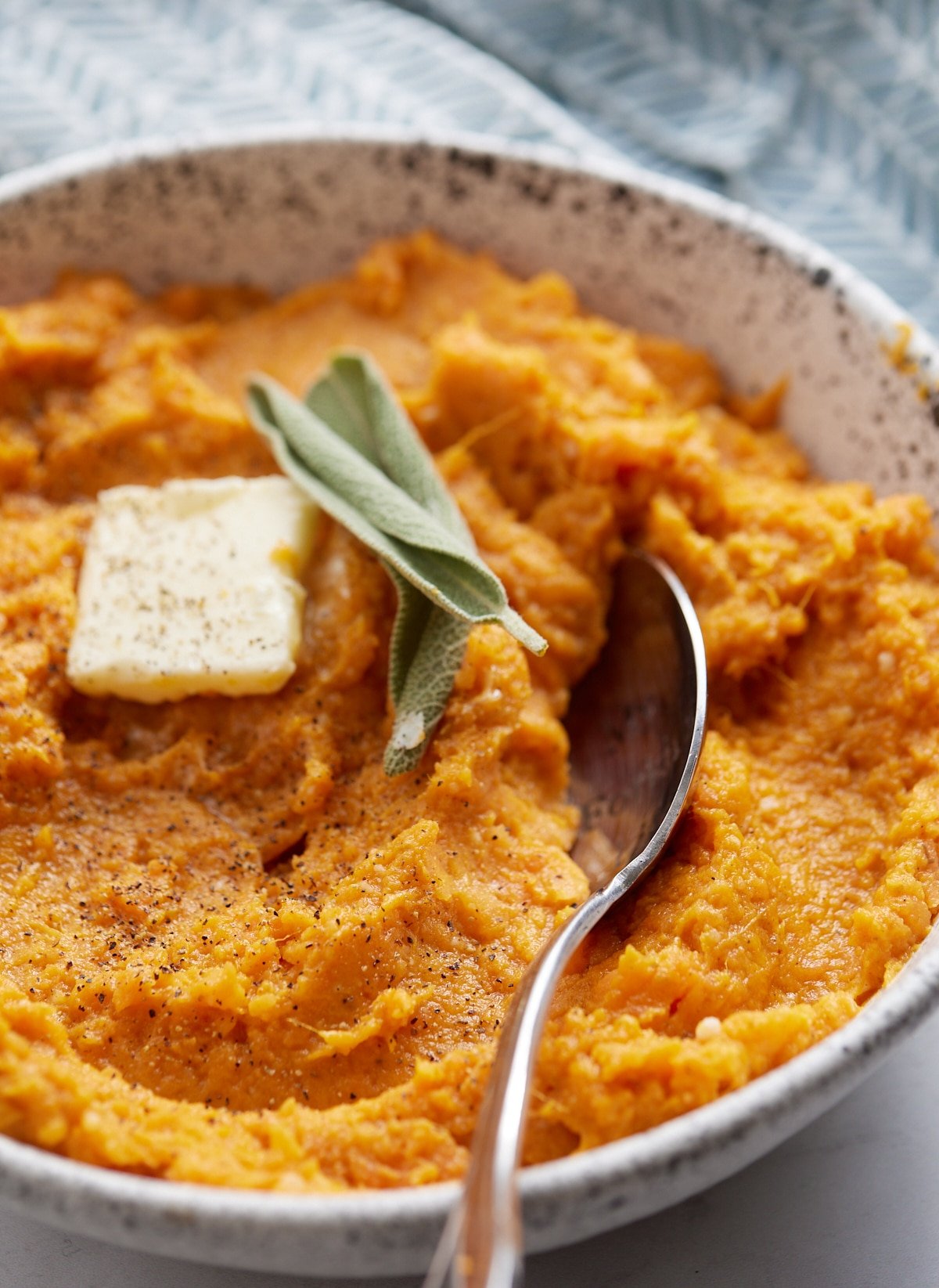 sweet potato in bowl with spoon sticking out topped with sage