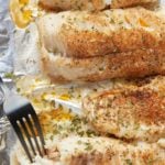 Baked fish fillets on a baking sheet with a fork.