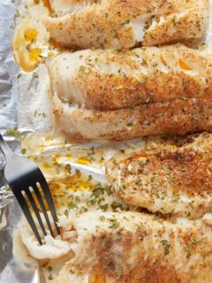 Baked fish fillets on a baking sheet with a fork.