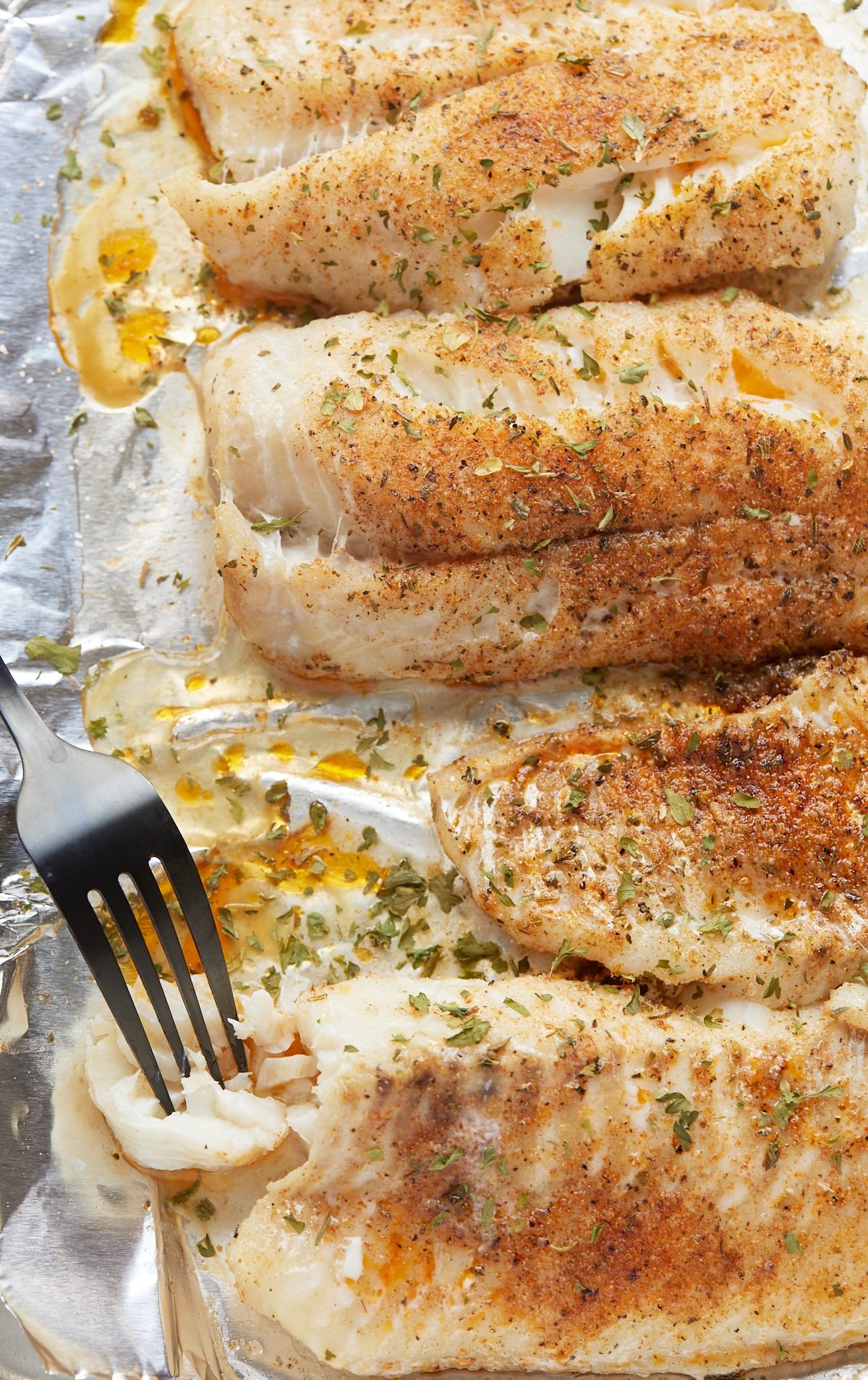 Baked fish fillets on a baking sheet with a fork.