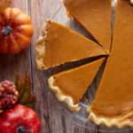 A homemade pumpkin pie cut into slices on a wooden table.