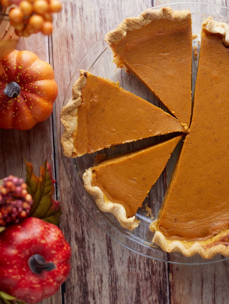 A homemade pumpkin pie cut into slices on a wooden table.