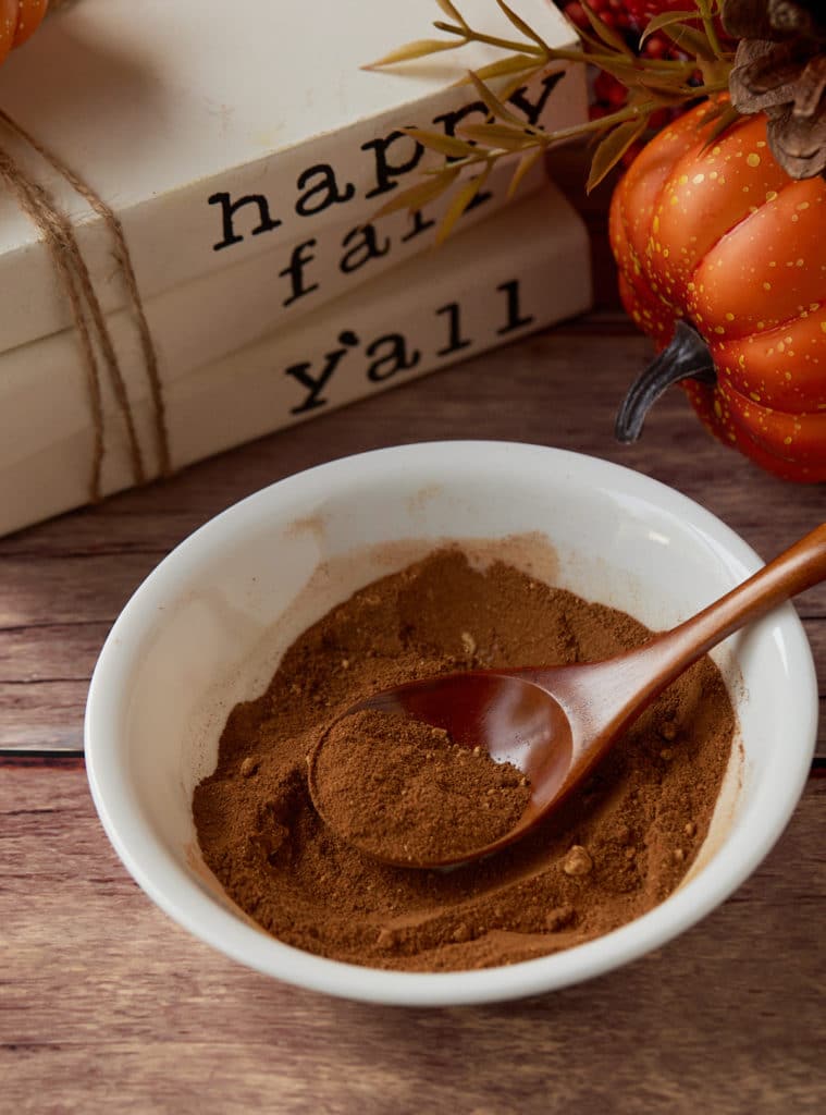 Pumpkin pie spice in a white bowl with a wooden spoon.