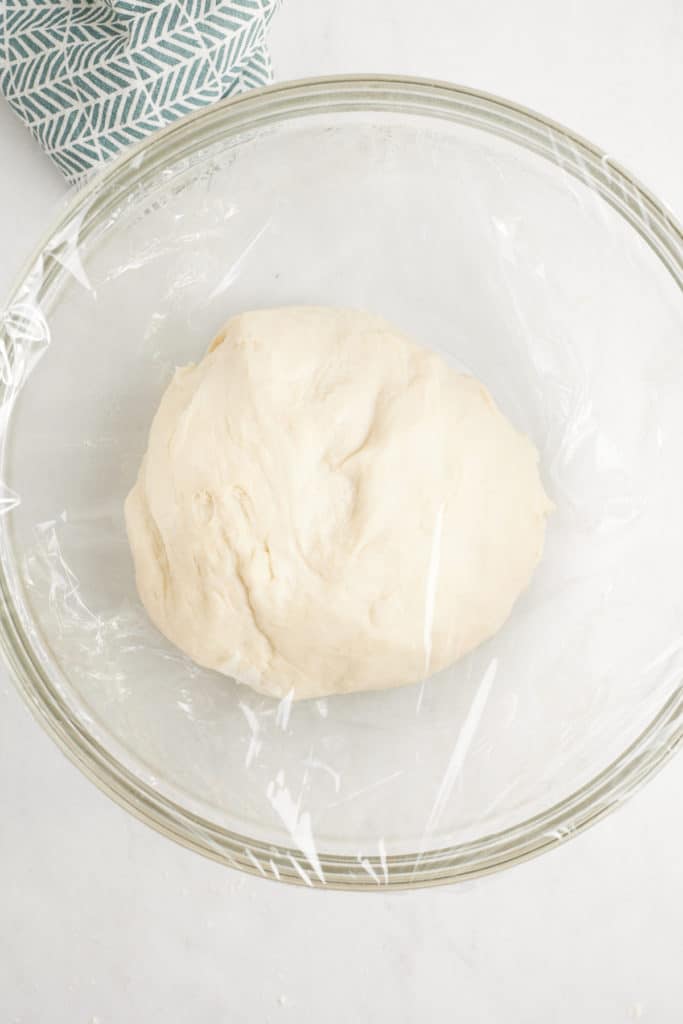 dough in glass bowl covered with plastic wrap