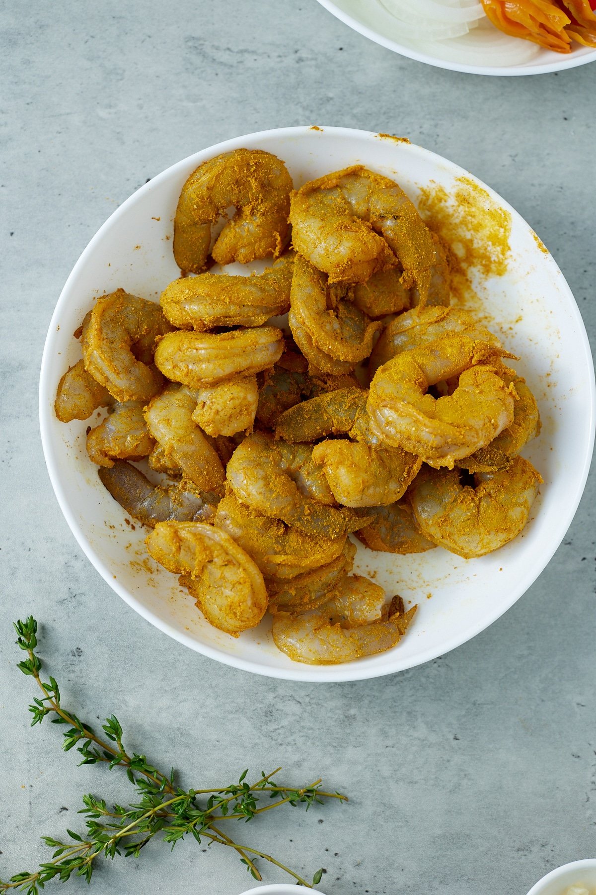 raw shrimp seasoned with curry powder in white bowl
