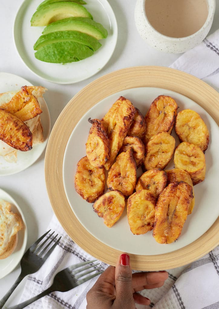 A hand placing a plate of air fried plantains on a table.