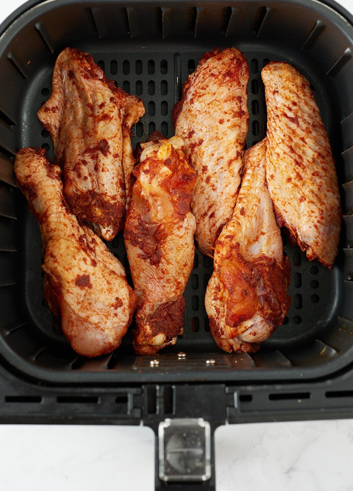 Uncooked wings in the air fryer basket.