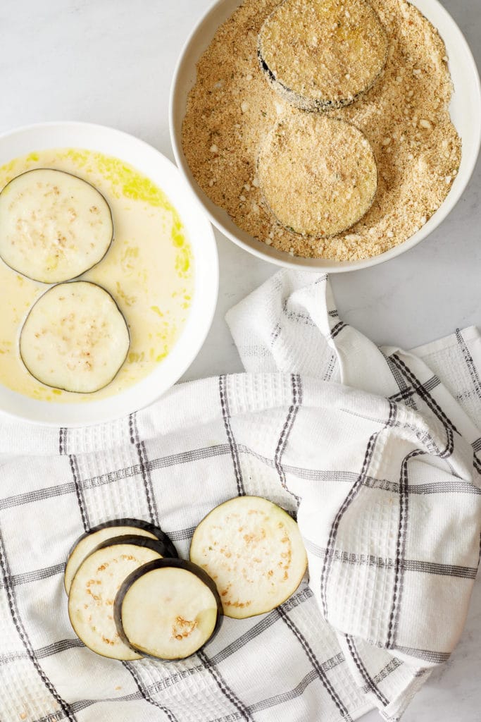 Eggplant rounds being coated in the egg and breadcrumbs.