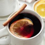 Mulled wine served in a mug with a cinnamon stick and orange slice.