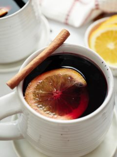 Mulled wine served in a mug with a cinnamon stick and orange slice.