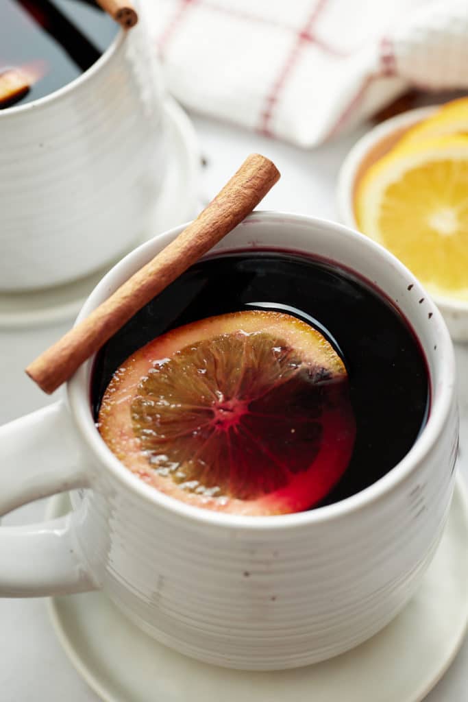 Mulled wine served in a mug with a cinnamon stick and orange slice.