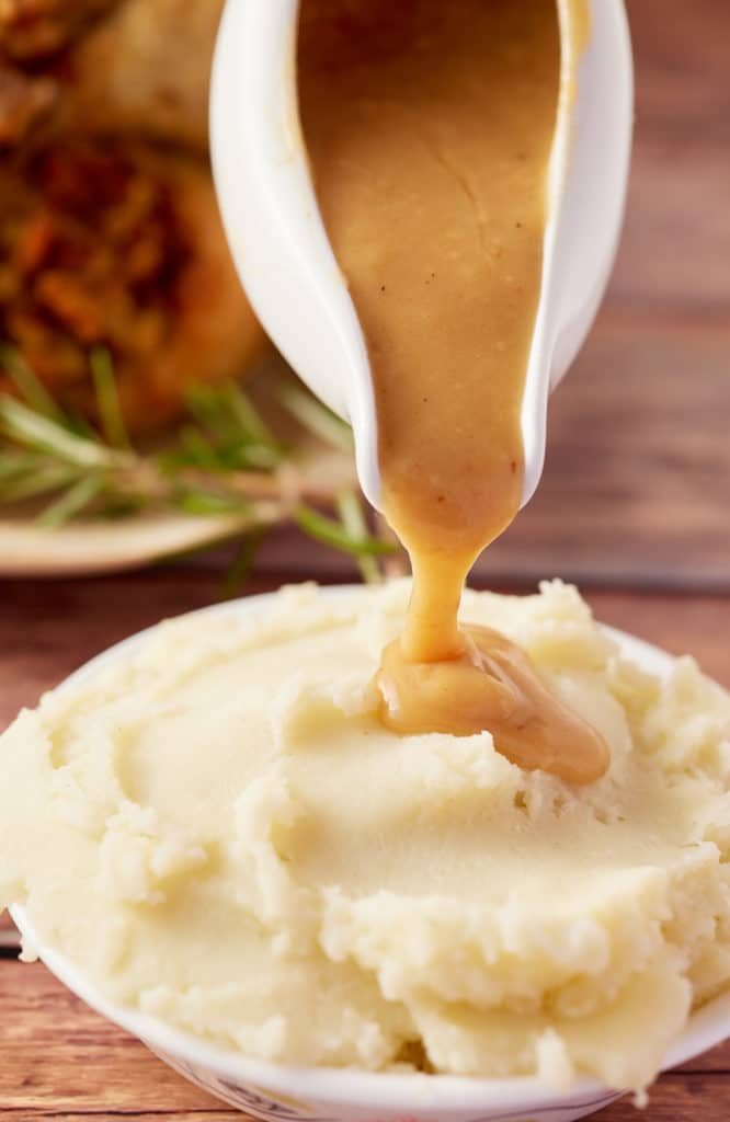 Dripping gravy being poured over mashed potato.