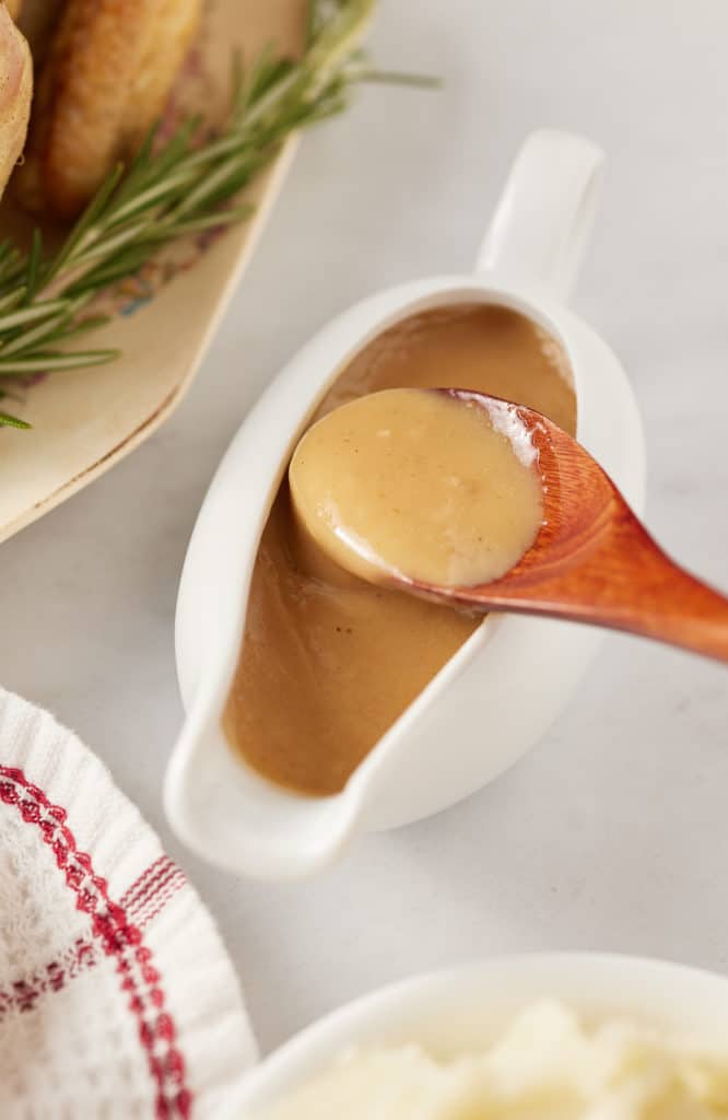 The dripping gravy in a gravy boat with a wooden spoon.