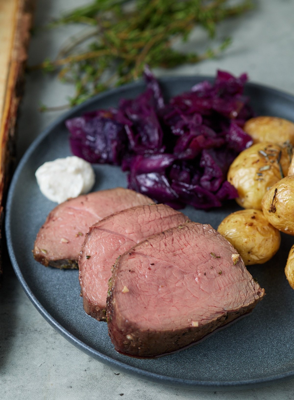 Three slices or air fryer beef tenderloin on a plate with potatoes and red cabbage.