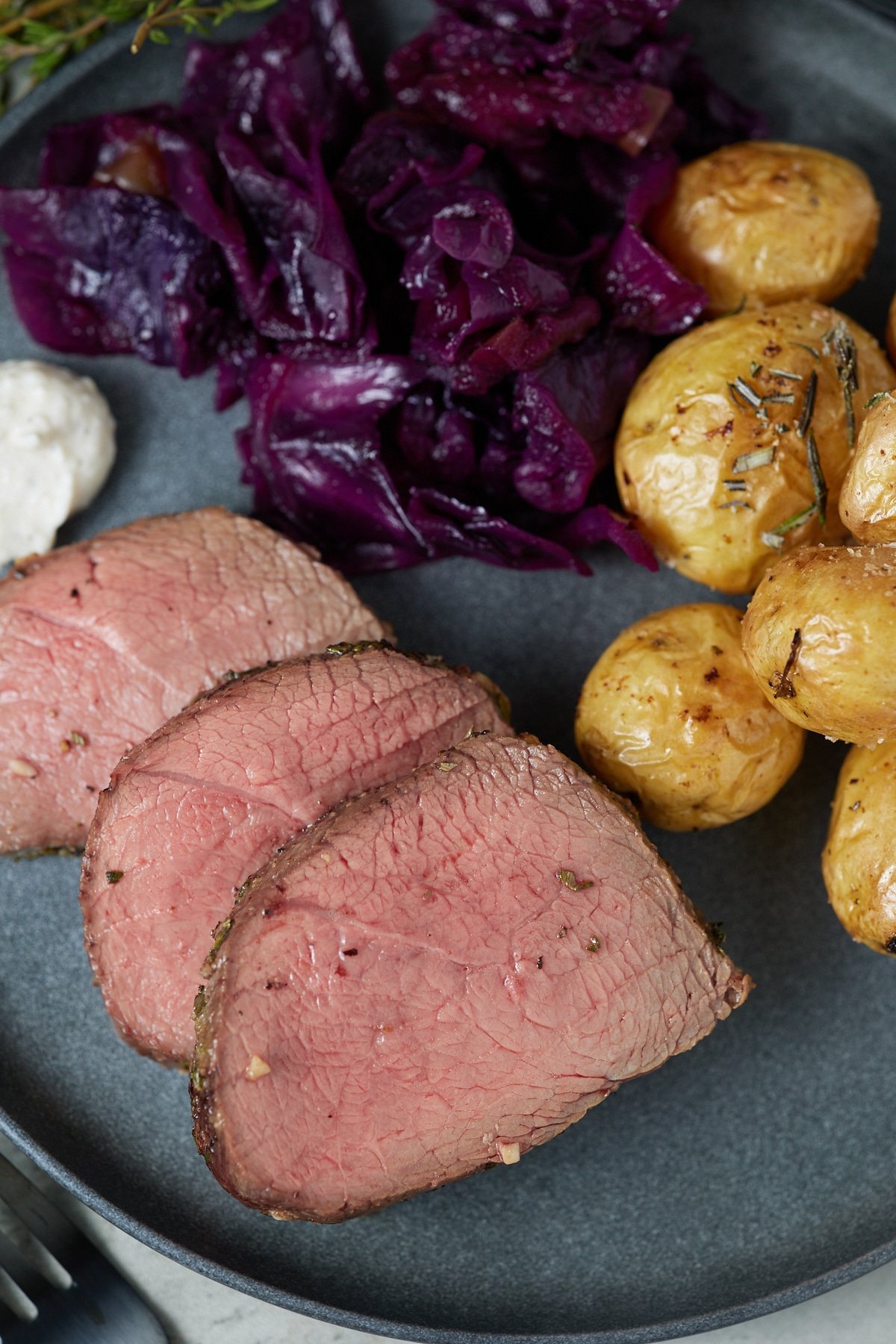 Close up of sliced beef on a plate with vegetable and potato sides.