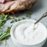 Close up of horseradish sauce in a bowl net to fresh herbs.