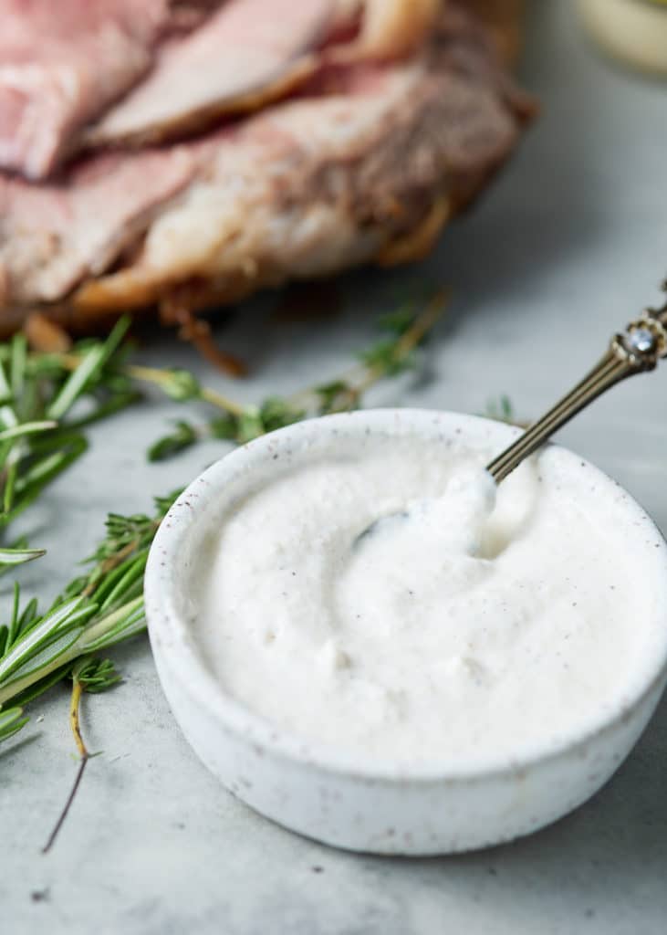 Close up of horseradish sauce in a bowl net to fresh herbs.