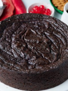 jamaican black cake on table with cherries and drink behind it