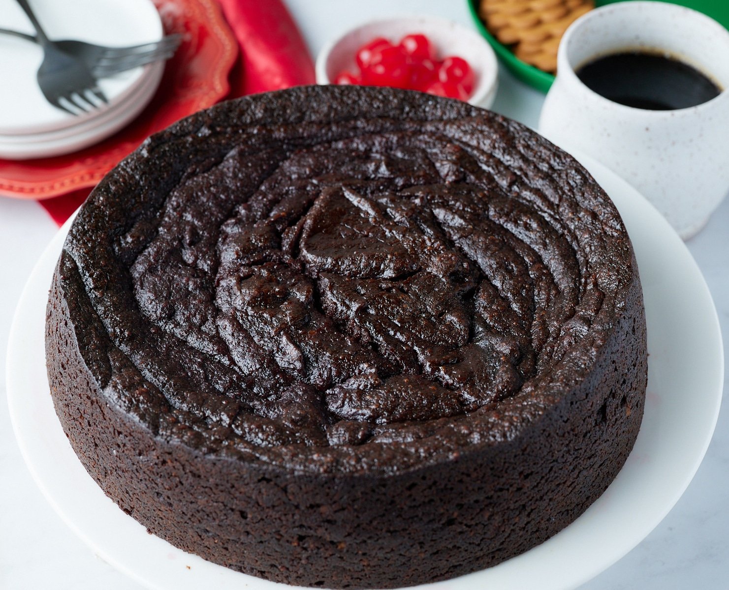 jamaican black cake on table with cherries and drink behind it