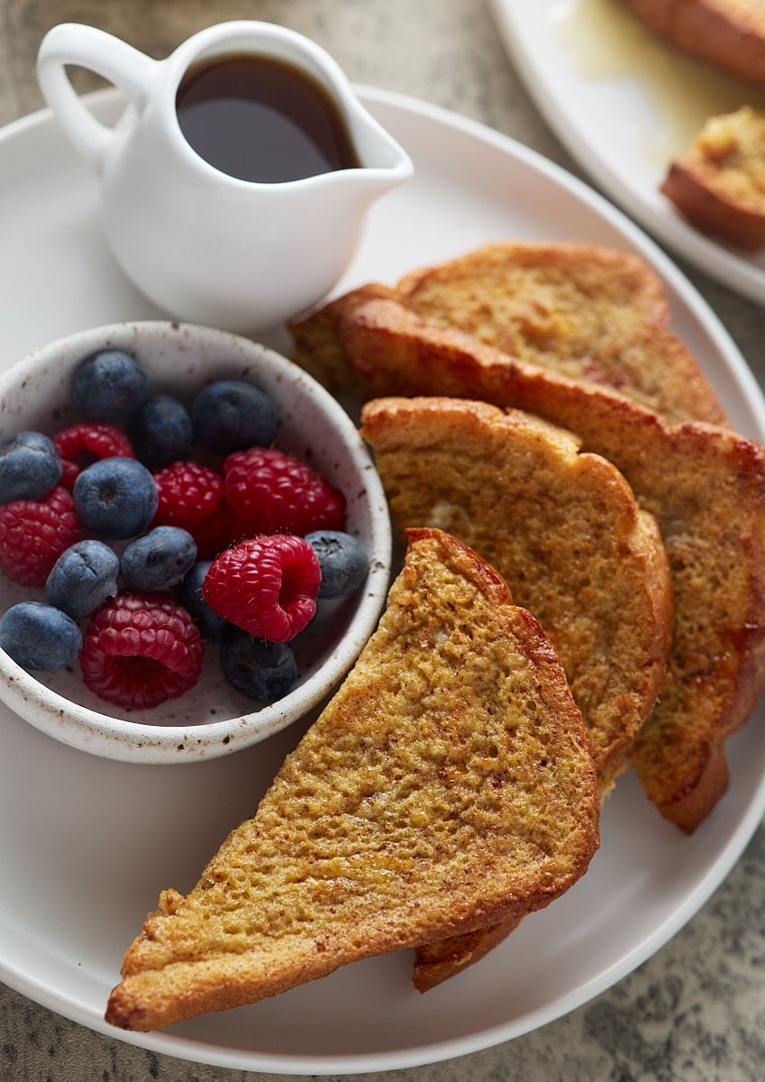Slices of air fryer French toast on a white plate next to a bowl of fresh berries.