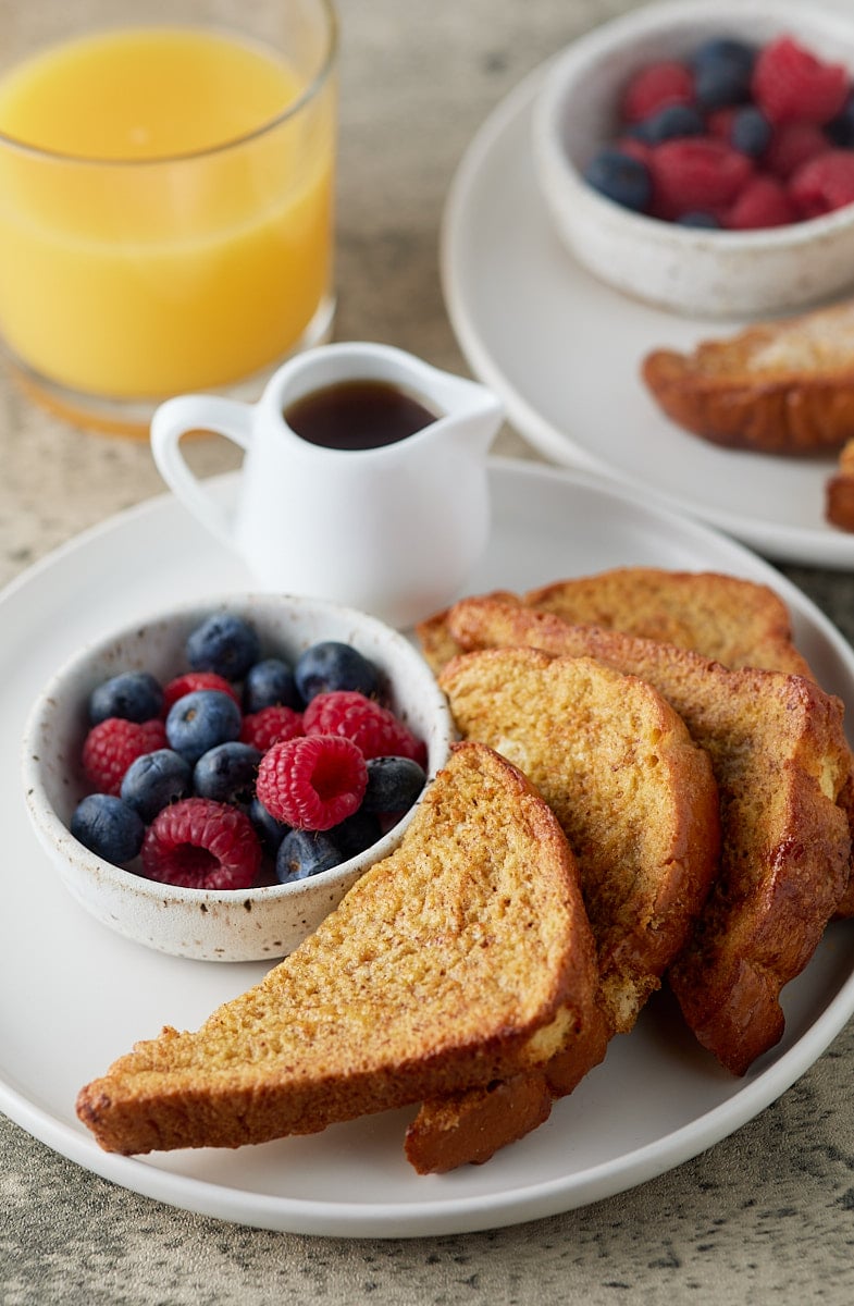 French toast, fresh berries and a jug of syrup on a white plate.