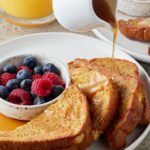 Maple syrup being poured from a white jug over air fryer French toast.